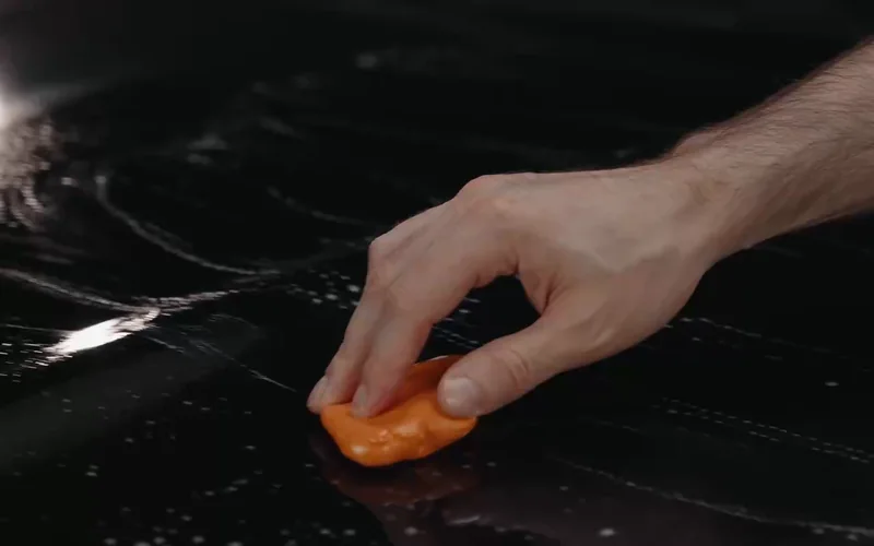 A clay bar moving across wet black vehicle paint