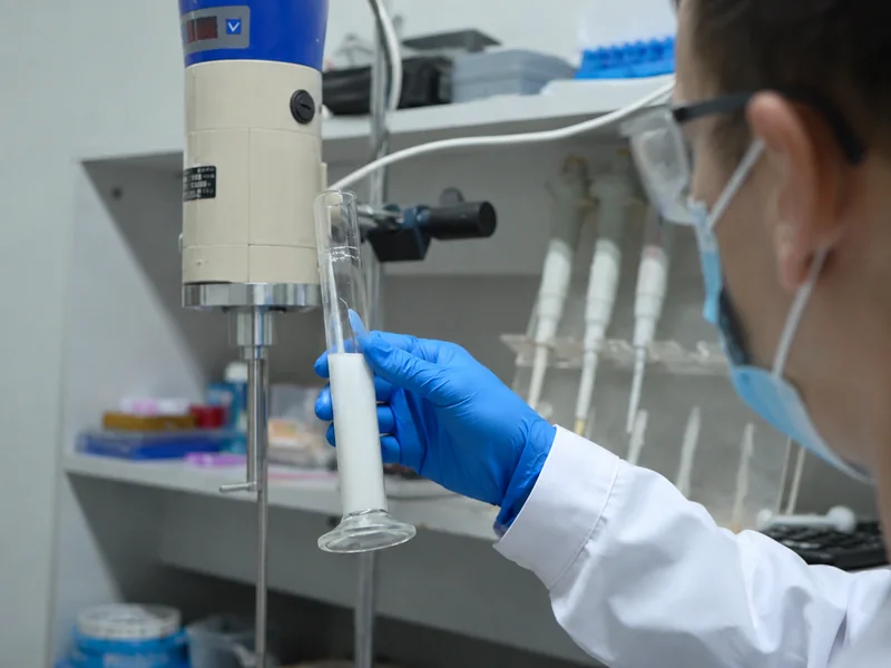 AI-generated close-up of a gloved hand holding a coating sample beside a laboratory mixer.