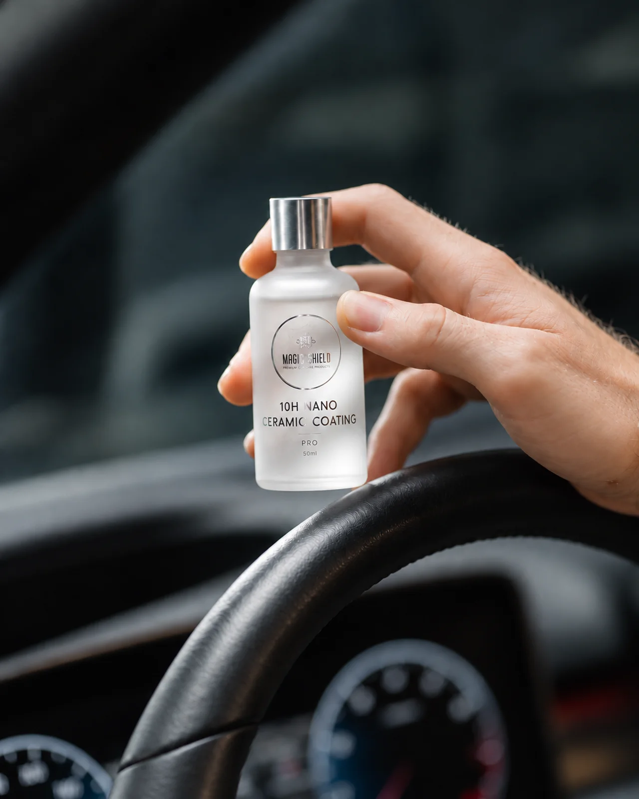 A hand holding the 50 mL Magic Shield PRO 10H bottle inside a vehicle