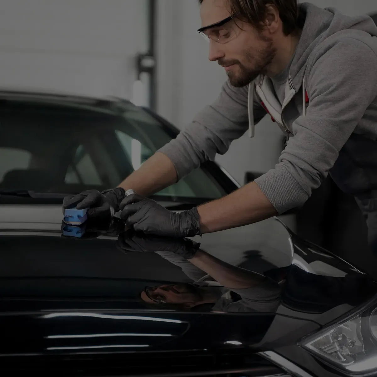 A technician applying a coating to a dark vehicle panel.