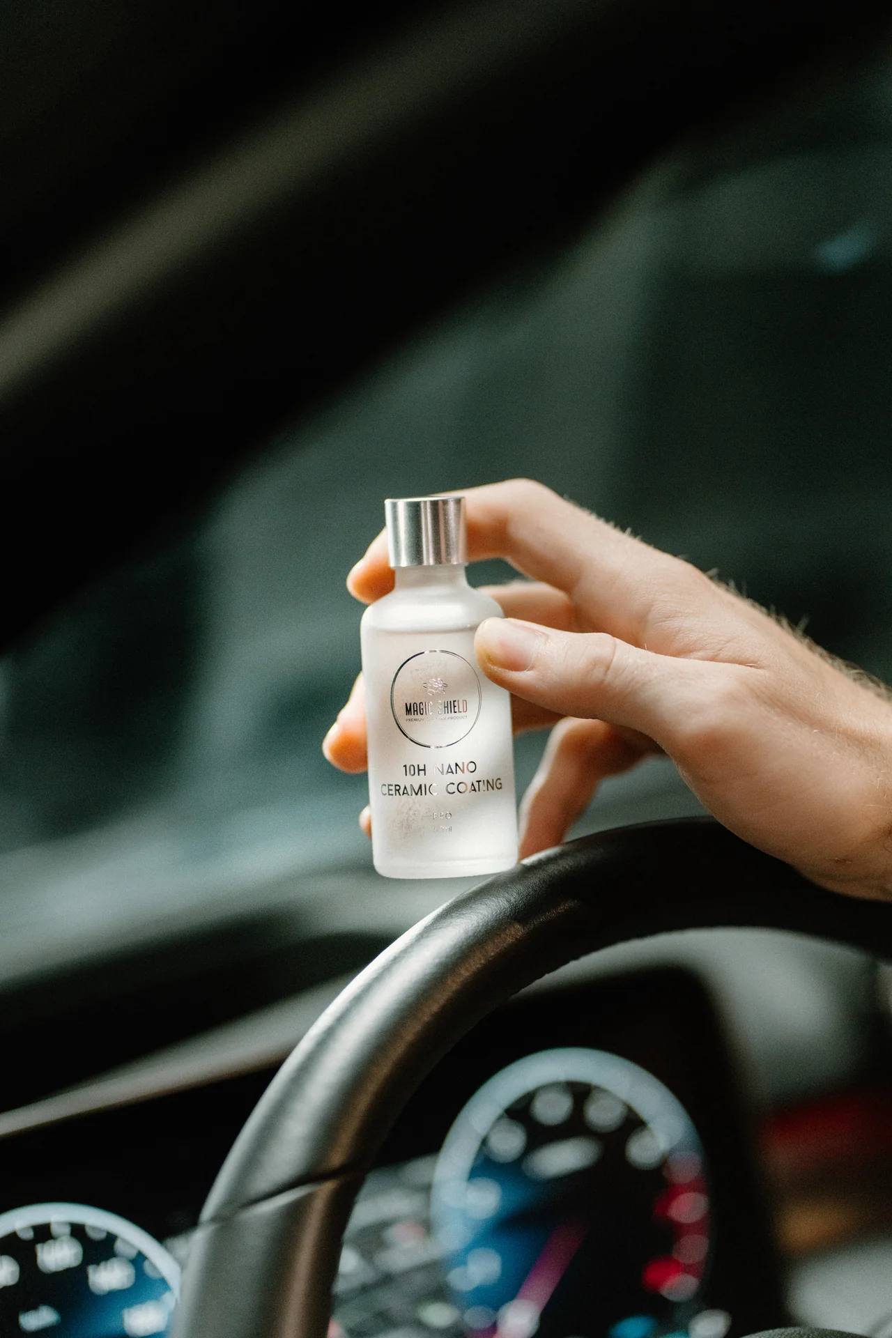A hand holding the 50 mL Magic Shield PRO 10H bottle inside a vehicle