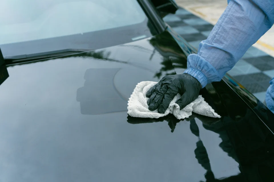 A gloved hand levelling coating on a dark vehicle hood with a microfiber towel